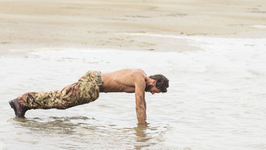 man in camo doing push ups on shore